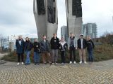 Dziewięcioro licealistów stoi w rzędzie przed pomnikiem trzech krzyży. Wszyscy są w kurtkach. W tle wysoki budynek.