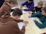 Pięcioro uczniów szkoły podstawowej siedzi przy stoliku i rozwiązuje na kartce zadania.