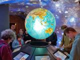 Grupa gimnazjalistów stoi dookoła wyświetlanego kolorowego hologramu kuli ziemskiej