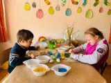 Dwoje dzieci ozdabiajacych kolorowymi pisakami jajka wycięte z kartonu