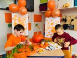 Dwoje uczniów ubranych na pomarańczowo siedzi przy stoliku. Na stoliku pomarańczowe warzywa i owoce.