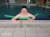 Uśmiechnięty chłopiec w basenie z długą zieloną piankową rurką