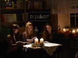 Trzy uczennice liceum siedzą przy stoliku i czytają książkę. Na stole stoją dwie zapalone swiece.