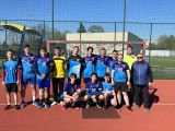 Drużyna chłopców z liceum w strojach sportowych stoi w bramce. Dziesięciu chłopaków stoi, trzech kuca. Obok stoi mężczyzna...