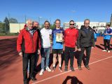 Na boisku w rzędzie stoi pięciu mężczyzn i licealista w niebieskim stroju sportowym. Chłopak trzyma dyplom.