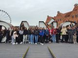 Na chodniku stoi duża grupa uczniów liceum. Za mini duży napis "Gdańsk", W tle budynek z czerwonej cegły.