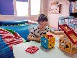Uśmiechnięty chłopiec układa figury w kostce sześciennej, w tle basen z kolorowymi piłkami