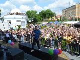 Na scenie chłopak w niebieskiej koszuli śpiewa do mikrofonu. Przed sceną tłum ludzi.