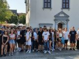 Duża grupa uczniów liceum stoi na chodniku przed białym budynkiem.