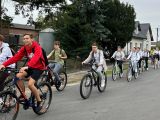 Uczniowie liceum, szkoły podstawowej i dorośli jadą na rowerach asfaltową drogą. W tle drzewa.