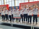 Dziewięciu mężczyzn w dresach sportowych i srebrnymi medalami na szyi stoi na podium
