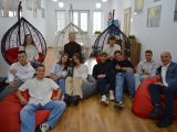 Na czerwonych i szarych pufach siedzi dziesięcioro uczniów liceum oraz mężczyzna w granatowej mawynarce. W tle okno.