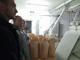 Troje gimnazjalistów w wysokim pomieszczeniu. Obok duże papierowe worki wypełnione zbożem
