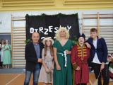 Pośrodku sali gimnastycznej w rzędzie stoi męzczyzna, trzech chłopaków w przebraniach i dziewczyna w kapeluszu.