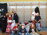 Na sali gimnastycznej przy drabinkach siedzi grupa uczniów liceum przebranych w różne kolorowe stroje, kilkoro licealistów...