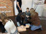 Trzy uczennice liceum pochylają się nad manekinem i uciskają mu klatkę piersiową.
