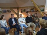 W sali na krzesłach w rzędzie siedz mężczyzna, dwie kobiety, dziewczyna i dwóch chłopców. Wszyscy są skupieni.