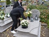 Uczeń liceum w czarnym stroju pochyla się nad grobem i zapala znicz. Obok stoi chłopak.