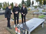 Trzech uczniów liceum w czarnych ubraniach stoi przy grobie na cmentarzu.