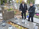 Dwóch uczniów liceum w czarnych ubraniach stoi przy grobie i zapala znicz.