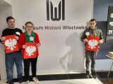 Troje uczniów stoi na tle logo Muzeum Historii Włocławka. W rękach trzymają wizerunek orła.