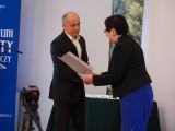 Mężczyzna w garniturze otrzymuje od kobiety dyplom. Kobieta składa mu gratulacje.