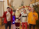 Troje uczniów stoi z Mikołajem. W tle dekoracje świateczne