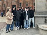 Ośmioro licealistów stoi przy pomniku Mikołaja Kopernika. W tle budynek kościoła z cegły.
