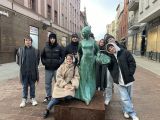 W uliczce miasta dziewięcioro uczniów licuem stoi przy niebieskim pomniku kobiety.