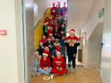 Dzieci siedzą na schodach, na głowach mają czapki Mikołaja. Przed nimi na talerzyku leżą ciastka, w szklance mleko.