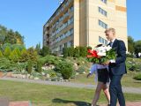 Uczeń liceum w garniturze niesie biało-czerwone kwiaty. Obok niego idzie dziewczyna w białej bluzce.