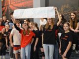 Grupa uczennic liceum w czarnych koszulkach trzyma nad głowami biały baner z napisem.