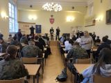 Sala konferencyjna, wypełniona uczestnikami konkursu. Na ścianie logo LMK.