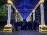 Grupa młodzieży pod oświetlonym kolorowymi lampkami dachem, wsparym na kolumnach.