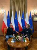 Dwaj chłopcy, siedzący przy niewielkim stoliku. W tle flagi Polski i Unii Europejskiej.