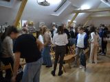 W sali między krzesłami stoją uczniowie liceum i szkoły podstawowej (około 50 osób). Rozmawiają w parach.
