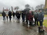 Na dziedzińcu przed  budynkiem szkoły stoi grupa ludzi w różnym wieku.