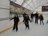 Duża grupa uczniów liceum jeździ na łyżwach po krytym lodowisku. Wszyscy są uśmiechnięci.