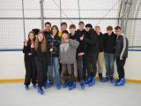 Duża grupa licealistów stoi na lodowisku przy barierce. Wszyscy mają łyżwy na nogach.