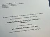 Na białej kartce czarny tekst z gratulacjami dla szkoły. Kartka w granatowe okładce.