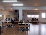 Aula szkolna. Dzieci w trzyosobowych zespołach rozwiązują zadania przy stolikach.