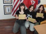 Trzy nastolatki trzymające w rękach koperty na tle flag USA, GB i Polski