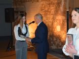 Mężczyzna w garniturze wręcza świdectwo uczennicy liceum w białej bluzce.