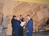 Dwóch mężczyzn wręcza świdectwo uczeniowi liceum  w garniturze.