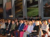 Uczniowie i nauczyciele liceum siedzą na krzesiałach w rzędach w sali gimnastycznej.