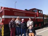 Dwie kobiety i troje uczniów przed wielką, czerwoną lokomotywą. Chłopiec po prawej siedzi na wózku inwalidzkim
