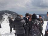 Na pierwszym planie grupa nastolaków w zimowych strojach. W tle ośnieżony górski szczyt.