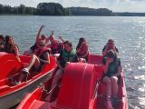 grupa nastolatków na czerwonych rowerkach wodnych. W tle tafla jeziora.