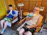 Dwoje uczniów siedzi w fotelach trzymając przy szyjach lecznicze  lampy Sollux