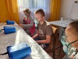 Troje uczniów w maskach na twarzy. Przed nimi inhalatory